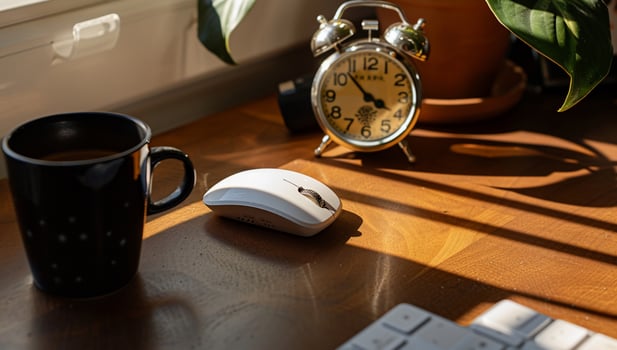 Cozy workspace with a coffee mug, wireless mouse, alarm clock, and potted plant photo