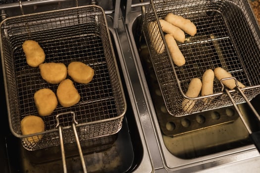 Fried snacks cooking in deep fryer with various shapes and sizes being prepared in a restaurant kitchen during busy afternoon hours photo