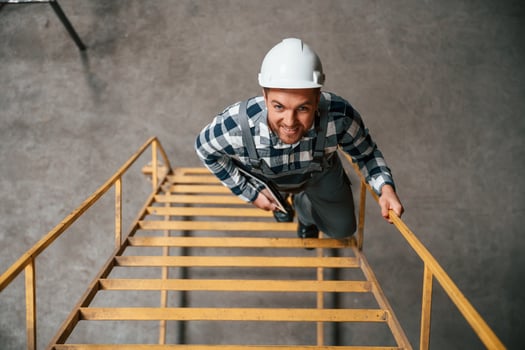Top view. Going up on the ladder. Factory male worker i,n uniform is indoors photo