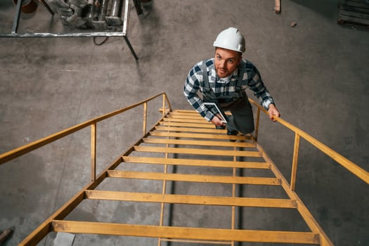 Top view. Going up on the ladder. Factory male, worker in uniform is indoors photo