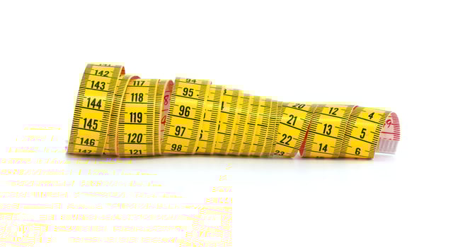 Bright yellow measuring tape coiled on a white surface displays various inch and centimeter markings photo