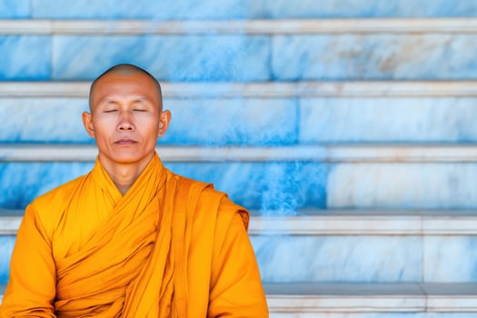 Buddhist monk in saffron robes meditates peacefully at ancient temple steps surrounded by incense smoke photo