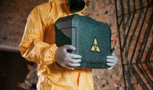 Case with ,biohazard sign in hands. Man dressed in chemical protection suit in the ruins of the post apocalyptic building photo