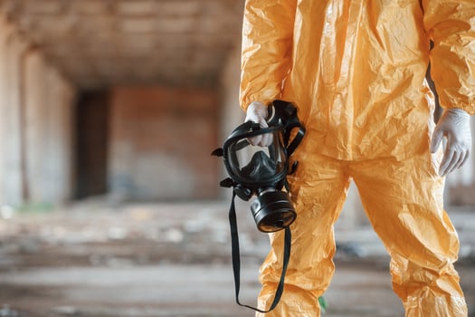 Holding gas mask. Man, dressed in chemical protection suit in the ruins of the post apocalyptic building photo
