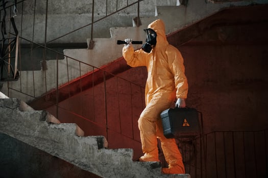 On stairs with flashlight and case. Man dressed in chemical protection suit in the ruins of the post apocalyptic building photo