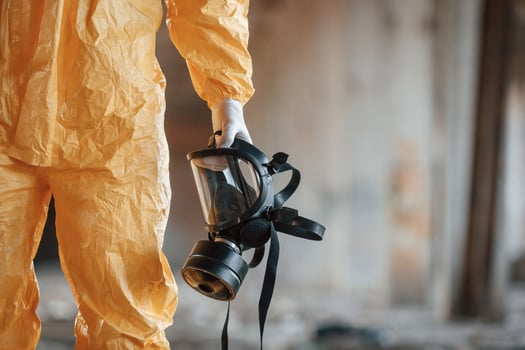 Holding gas mask. Man dressed in chemical protection suit in the ruins of the post apocalyptic building photo