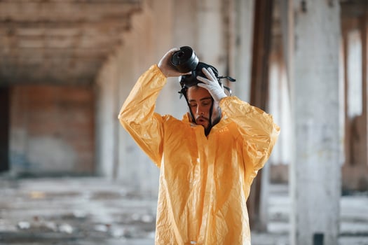 Taking off gas mask. Man dressed in chemical protection suit in the ruins of the post apocalyptic building photo
