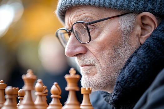 An older man wearing glasses and a hat is playing chess photo