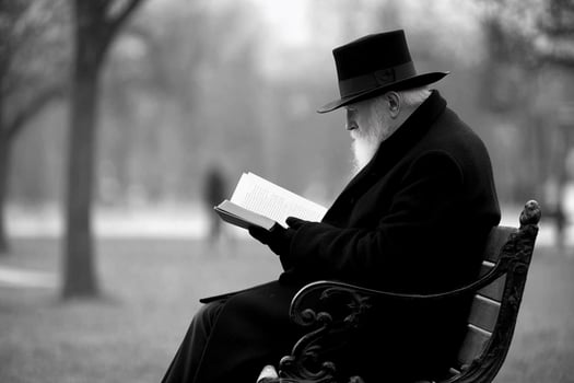 An old man in a hat and coat sitting on a park bench reading a book photo