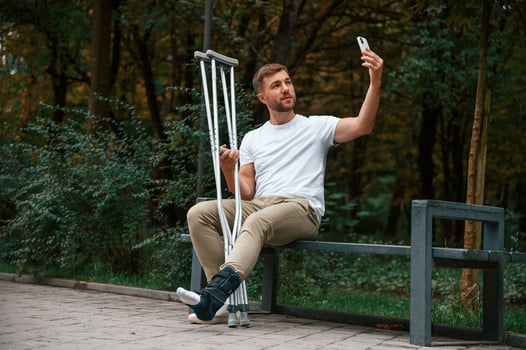 Making a selfie. Man ,with crutches is in the park outdoors. Having leg injury photo