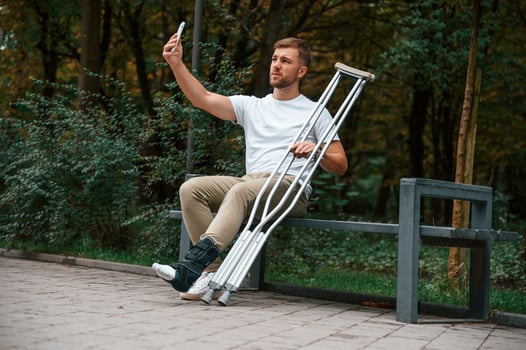 Making a selfie. Man with, crutches is in the park outdoors. Having leg injury photo