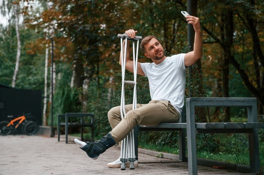 Making a selfie. Man with crutches ,is in the park outdoors. Having leg injury photo