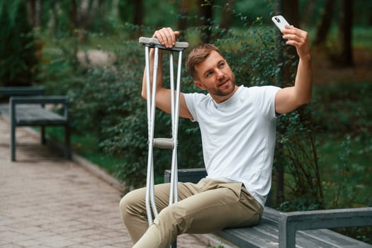 Man with crutches is in the park, outdoors. Having leg injury photo