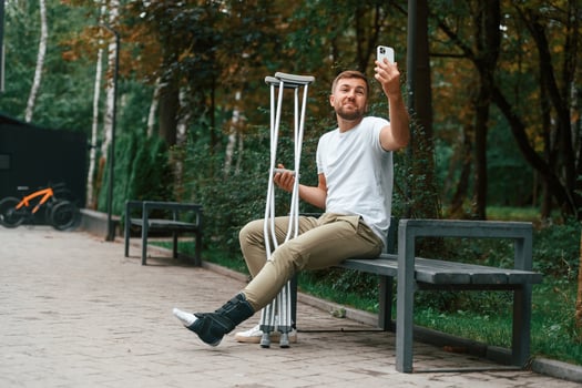 Using, smartphone ,to make selfie. Man with crutches is in the park outdoors. Having leg injury photo