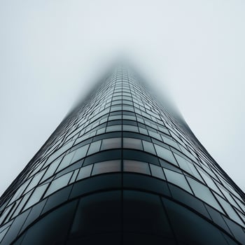 Modern skyscraper rising above fog. Low-angle view of a contemporary glass high-rise building penetrating a hazy atmosphere photo