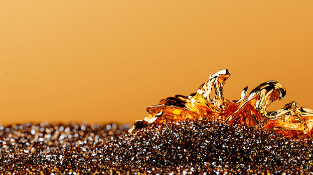 Close-up of shimmering golden liquid forming a wave against a warm orange background photo