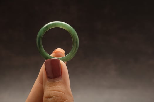 Close-up of hand holding a green jade ring on a black background photo