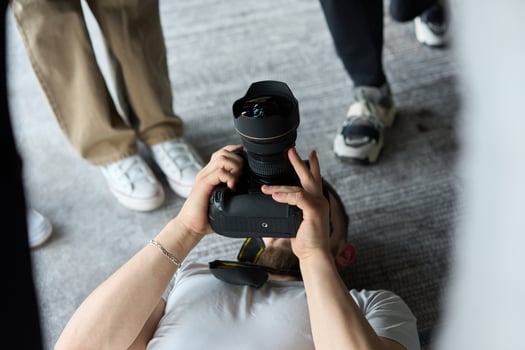 A photographer lies on the floor, capturing a heartfelt shot of a group of models embracing each other, showcasing their natural connection and joy in an intimate and creative moment photo