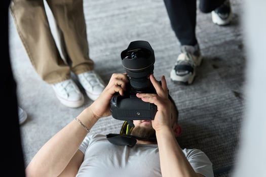 A photographer lies on the floor, capturing a heartfelt shot of a group of models embracing each other, showcasing their natural connection and joy in an intimate and creative moment photo
