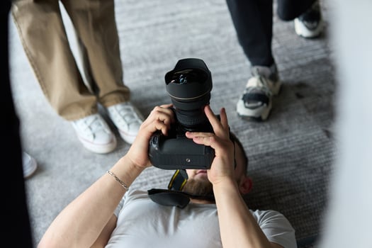 A photographer lies on the floor, capturing a heartfelt shot of a group of models embracing each other, showcasing their natural connection and joy in an intimate and creative moment photo