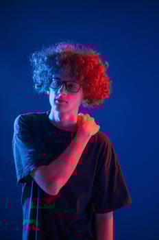 Posing ,for the camera. Young man with curly hair is indoors illuminated by neon lighting photo