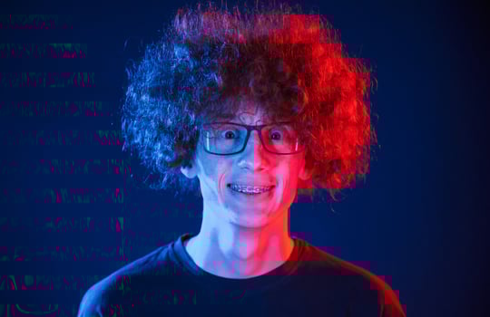 Portrait of young man ,with curly hair that is standing indoors, illuminated by neon lighting photo