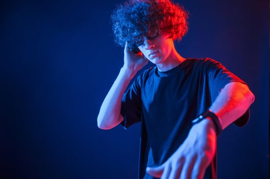 DJ is in the club. Young man with curly hair is indoors ,illuminated by neon lighting photo