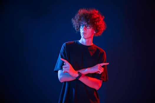 Posing for the camera. Young man with curly hair is indoors illuminated by neon lighting photo