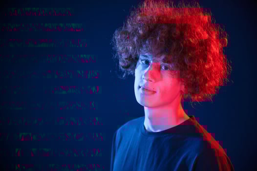 Portrait of young man with curly ,hair that is standing indoors, illuminated by neon lighting photo