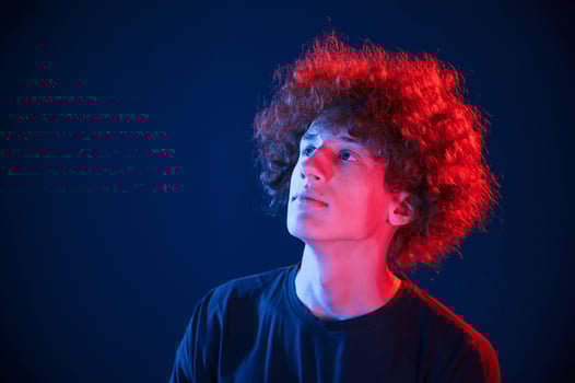 Looking up. Young man with curly hair is indoors illuminated by neon lighting photo