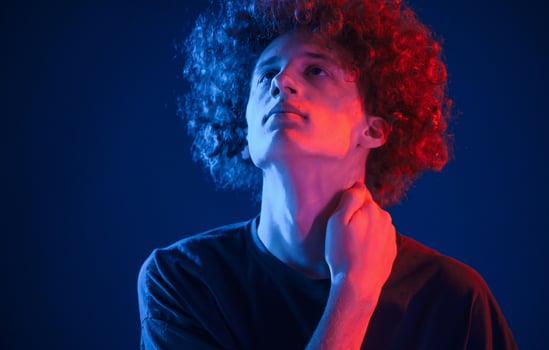 Looking up. Young man ,with curly hair is indoors illuminated by neon lighting photo