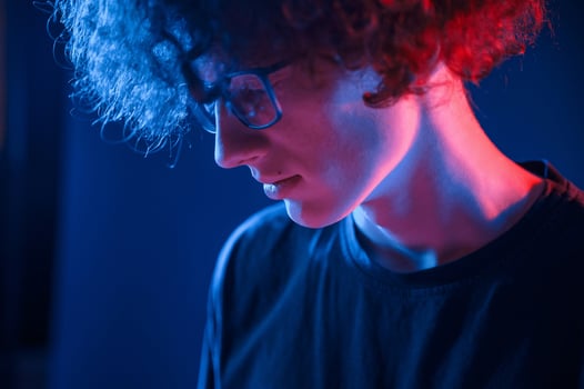 Looking down. Young man with curly hair is indoors illuminated by neon lighting photo