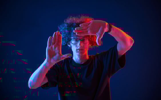 Gesture of making ,photo, pretending. Young man with curly hair is indoors illuminated by neon lighting photo