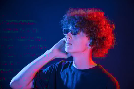 Red and blue colors. Young man with curly. hair is indoors illuminated by neon lighting photo