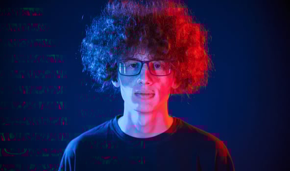 Serious facial expression. Young man with curly hair is indoors illuminated by neon lighting photo