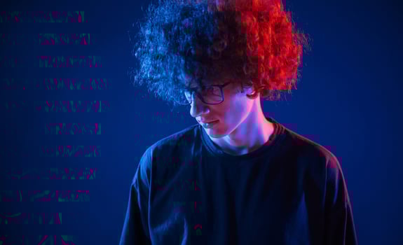 Looking down. Young .man with curly hair is indoors illuminated by neon lighting photo