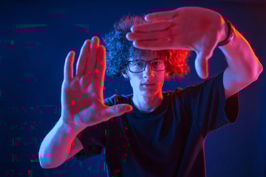 Gesture of making photo, pretending. Young man with curly hair is indoors illuminated by neon lighting photo