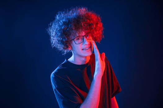 Conception of gossip. Telling a secret. Young man with curly hair is indoors illuminated by neon lighting photo