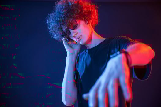 DJ is in the club.. Young man with curly hair is indoors illuminated by neon lighting photo
