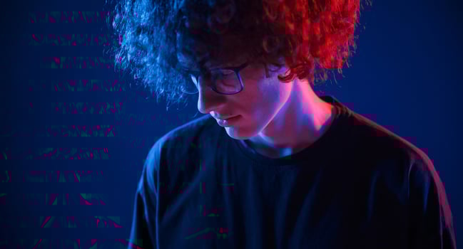 Looking down. Young man with, curly hair is indoors illuminated by neon lighting photo