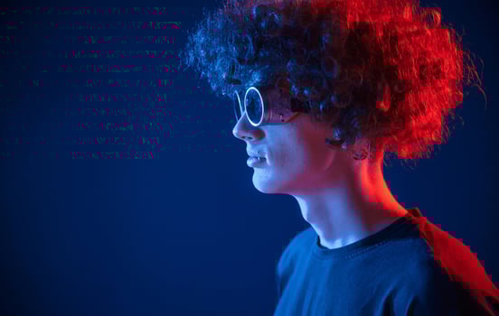 Vintage style glasses. Young man with curly, hair is indoors illuminated by neon lighting photo