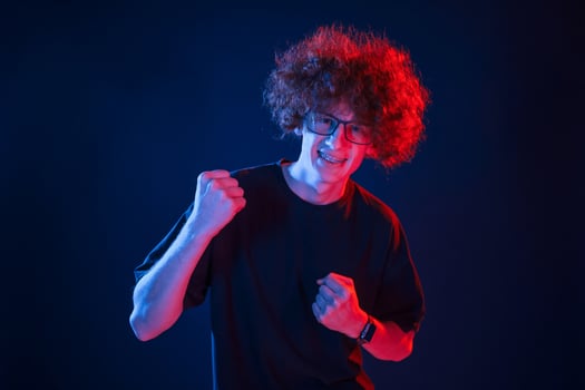 Feeling uplifting. Celebrating success. Young man with curly hair is indoors illuminated by neon lighting photo
