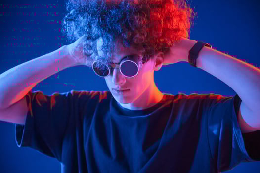 Vintage style, glasses. Young man with curly hair is indoors illuminated by neon lighting photo