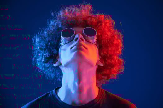 Portrait of young ,man with curly hair that is indoors illuminated by neon lighting. In retro eyewear photo