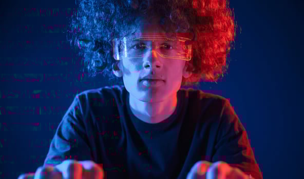 Gamer is focused by playing. Young man with curly hair is indoors illuminated by neon lighting photo