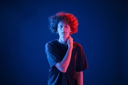 Posing ,for the camera. Young man with, curly hair is indoors illuminated by neon lighting photo
