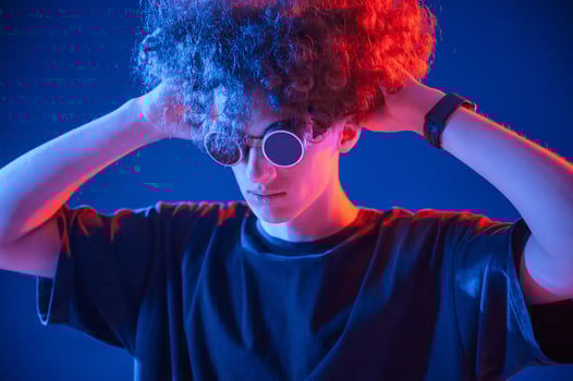 Looking ,through, the retro glasses. Young man with curly hair is indoors illuminated by neon lighting photo