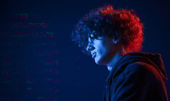 View from ,the side. Young man with curly hair is indoors illuminated by neon lighting photo