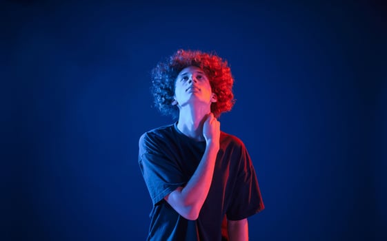Posing for the ,camera. Young man with curly hair is indoors illuminated by neon lighting photo