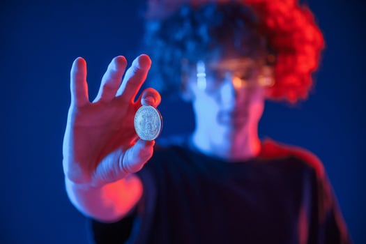 Holding bitcoin. .Young man with curly hair is indoors illuminated by neon lighting photo
